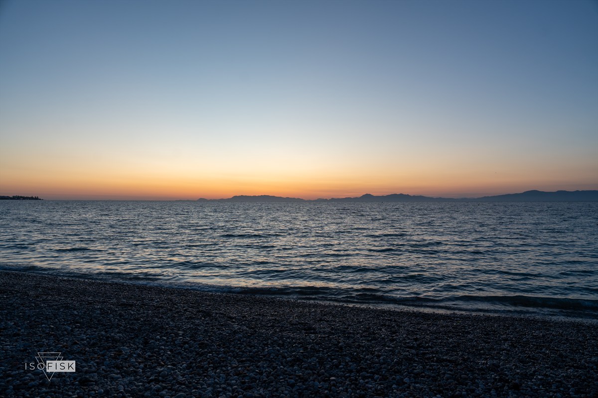 Calm sea and pebble beach beneath a warm sunset sky
