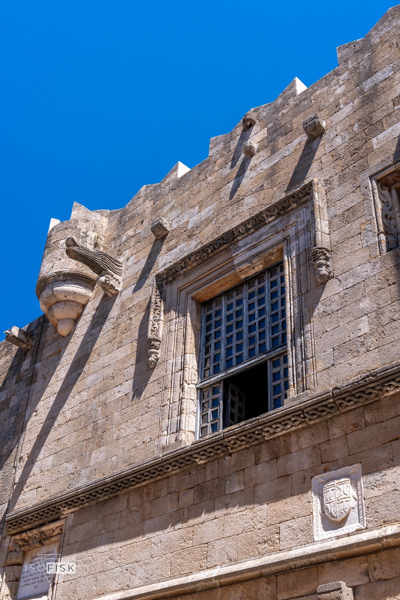 Looking up at a sunlit stone building and barred window