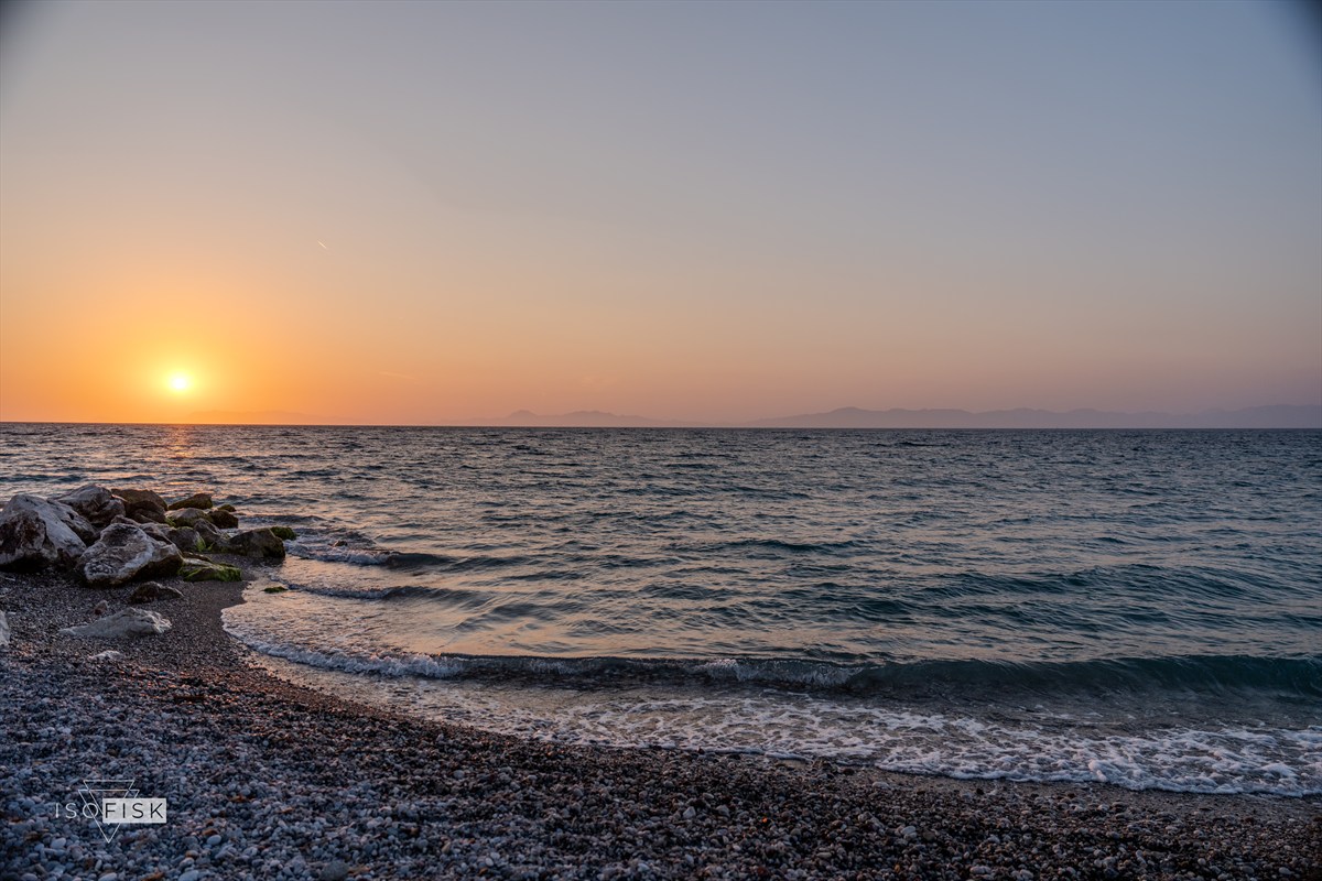 Sun setting over a pebble beach and gentle waves