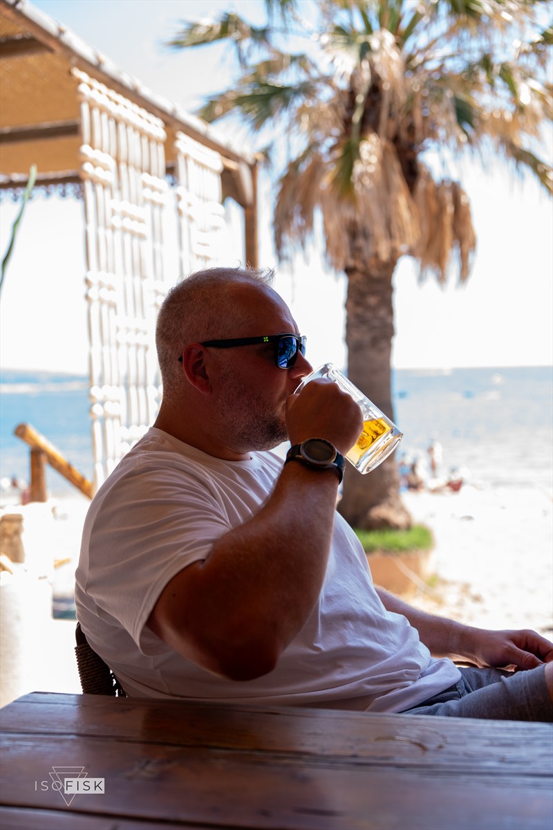 Person drinking at a beachside table with the sea behind