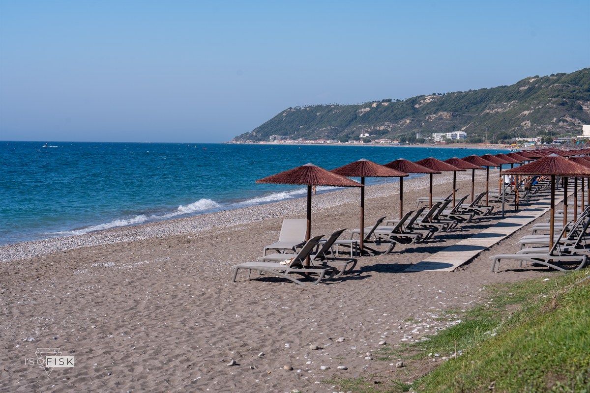 Rows of beach parasols beside blue water and coastal hills