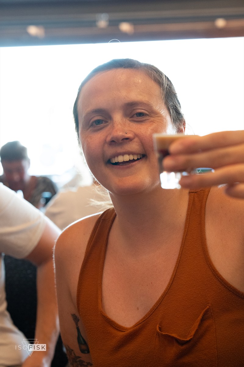 Person smiling and raising a small drink