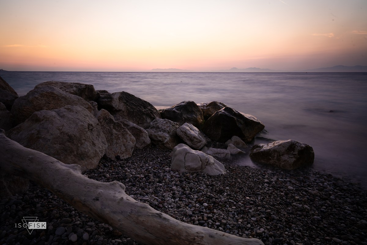 Soft water around rocks on a pebble beach at dusk